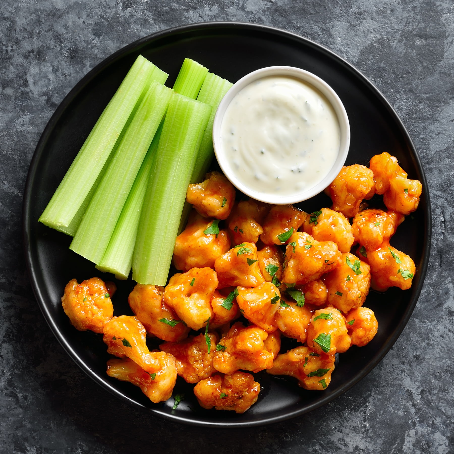Cauliflower buffalo wings on black plate over dark stone background. Top view, flat lay